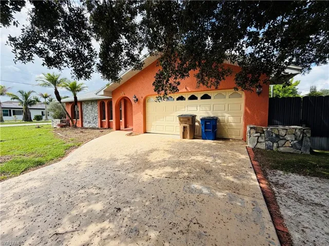 Coral stucco exterior with stone accents, arched entryway, two-car garage with decorative windows, and a stone-clad planter