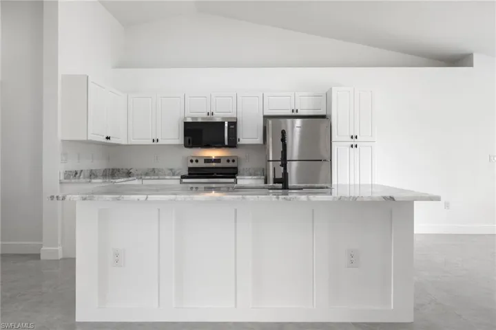 Kitchen featuring white cabinetry, light stone countertops, stainless steel appliances, lofted ceiling, and a center island