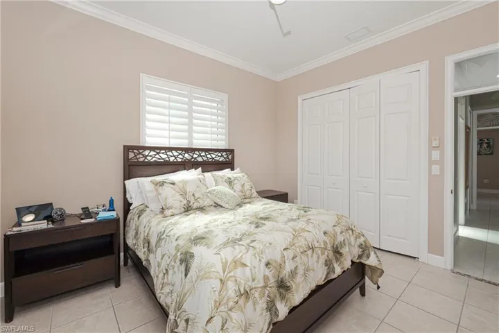 Tiled bedroom with ceiling fan, crown molding, and a closet