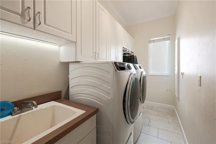 Washroom featuring cabinets, ornamental molding, sink, light tile patterned floors, and washing machine and dryer