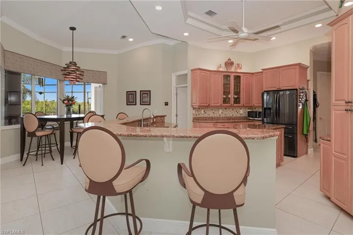 Kitchen featuring light stone counters, ornamental molding, ceiling fan, a kitchen island with sink, and fridge with ice dispenser
