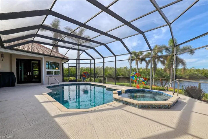 View of pool with glass enclosure, grilling area, an in ground hot tub, a water view, and a patio