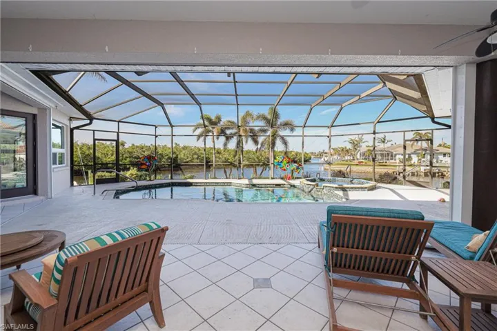 View of patio with glass enclosure, ceiling fan, a swimming pool with hot tub, and a water view