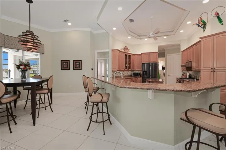 Kitchen with stone counters, ceiling fan, tasteful backsplash, stainless steel fridge with ice dispenser, and a breakfast bar