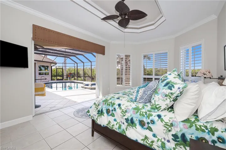 Tiled bedroom with ceiling fan, access to exterior, ornamental molding, and a tray ceiling