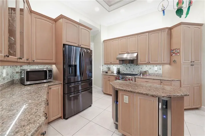 Kitchen featuring backsplash, appliances with stainless steel finishes, light brown cabinetry, light tile patterned floors, and ornamental molding