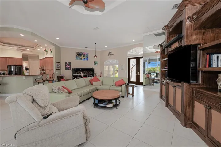 Living room with ceiling fan, french doors, a tray ceiling, light tile patterned flooring, and ornamental molding