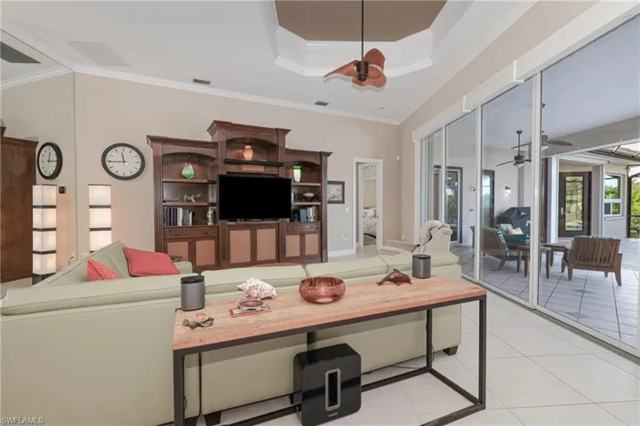 Living room featuring ceiling fan, light tile patterned flooring, ornamental molding, and a tray ceiling