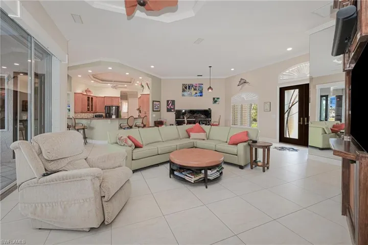 Tiled living room featuring french doors, a tray ceiling, ceiling fan, and crown molding