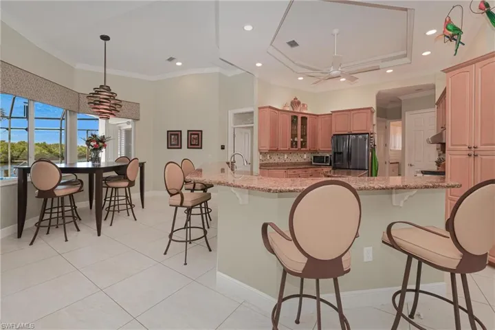 Kitchen featuring light stone countertops, appliances with stainless steel finishes, ornamental molding, a raised ceiling, and ceiling fan