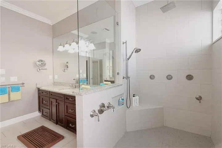 Bathroom with tile patterned floors, vanity, a tile shower, and crown molding
