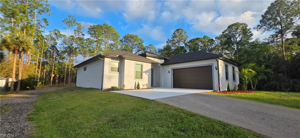 View of front of property with stucco siding, an attached garage, driveway, and a front lawn