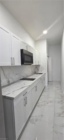 Kitchen featuring light marble finish floors, light stone counters, white cabinetry, tasteful backsplash, and cooktop