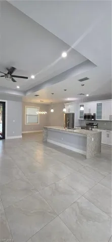 Kitchen featuring white cabinetry, hanging light fixtures, a spacious island, light stone countertops, and open floor plan
