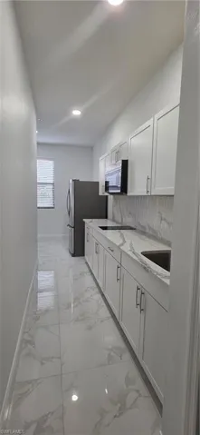 Kitchen featuring white cabinets, light stone countertops, light marble finish floors, freestanding refrigerator, and backsplash