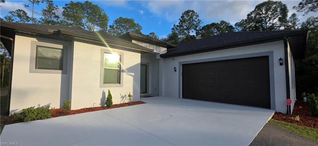 View of front of house with stucco siding, driveway, and a shingled roof