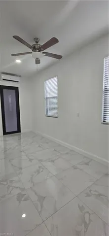 Unfurnished room with light marble finish flooring, an AC wall unit, and ceiling fan