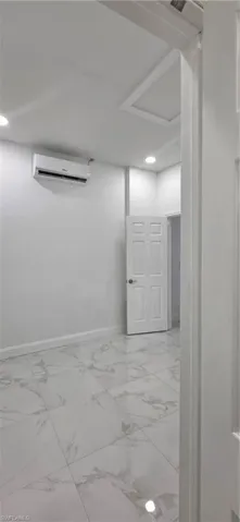 Below grade area with light marble finish floors, recessed lighting, and a wall unit AC
