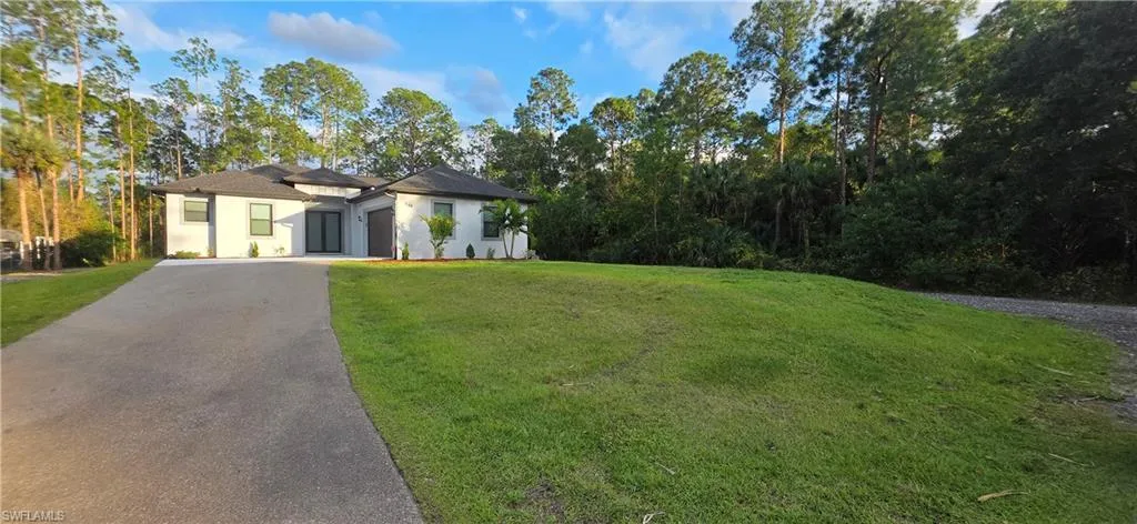 View of front of property featuring stucco siding, asphalt driveway, a front lawn, and view of wooded area