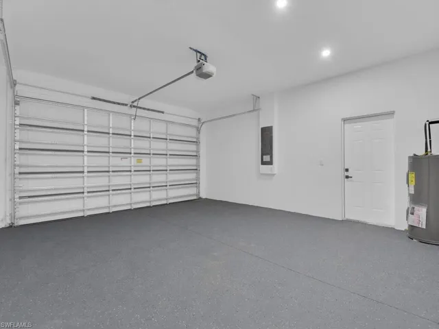 Garage with a garage door opener, electric panel, and electric water heater