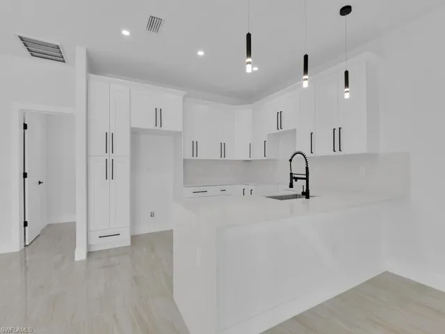 Kitchen with sink, kitchen peninsula, white cabinets, pendant lighting, and backsplash
