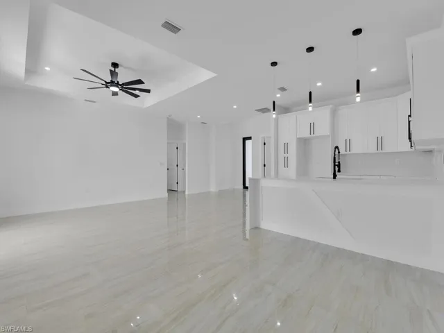 Unfurnished living room featuring ceiling fan, a raised ceiling, and sink