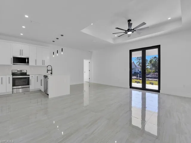 Unfurnished living room featuring a raised ceiling, sink, ceiling fan, and french doors