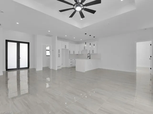 Unfurnished living room with french doors, ceiling fan, a raised ceiling, and sink