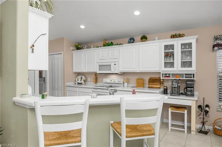 Kitchen with white appliances, light countertops, white cabinetry, a kitchen bar, and glass insert cabinets