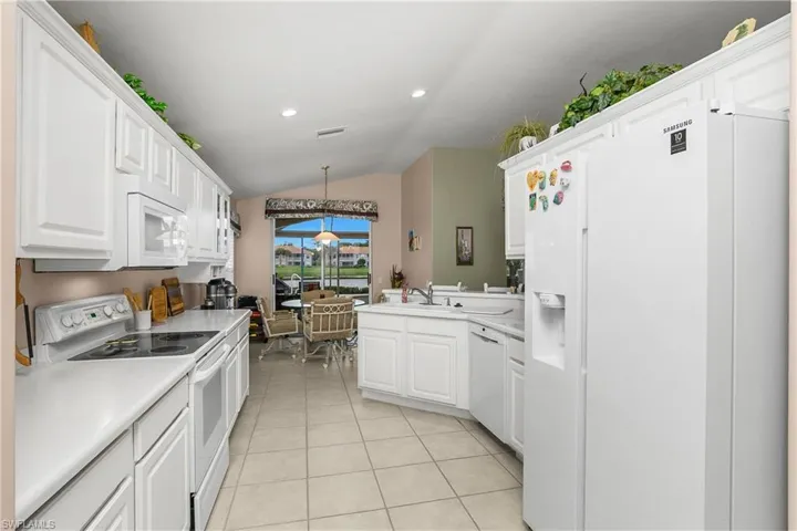 Kitchen with white appliances, decorative light fixtures, light countertops, vaulted ceiling, and white cabinets