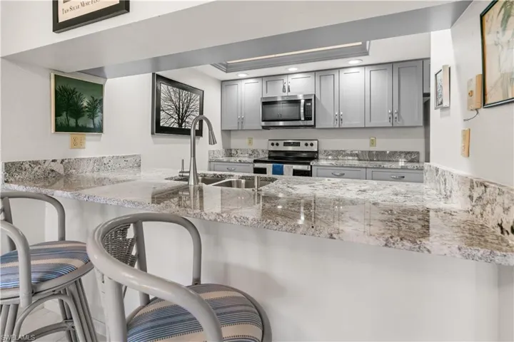Kitchen featuring a kitchen bar, appliances with stainless steel finishes, light stone countertops, sink, and gray cabinets