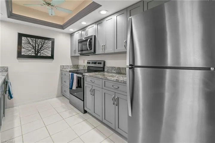 Kitchen featuring gray cabinets, light stone countertops, stainless steel appliances, and a tray ceiling