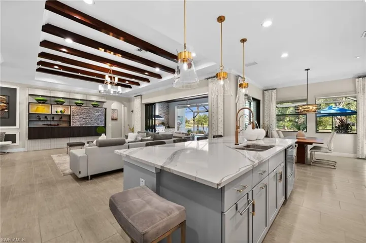Kitchen with pendant lighting, gray cabinetry, sink, light stone counters, and a center island with sink
