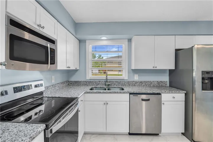 Kitchen featuring stainless steel appliances, white cabinets, light marble finish floors, and light stone counters