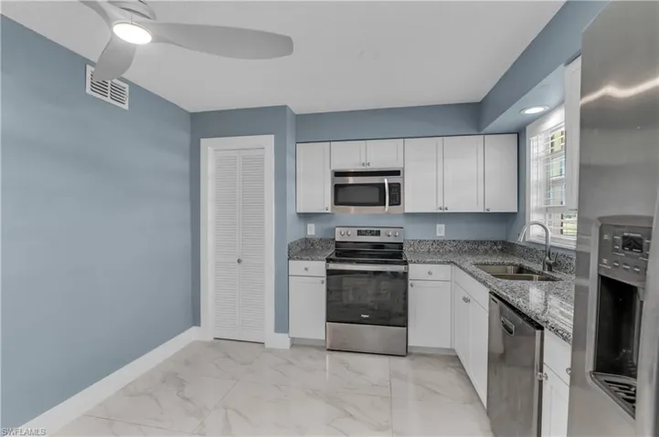 Kitchen featuring stainless steel appliances, light stone countertops, white cabinets, light marble finish floors, and a ceiling fan