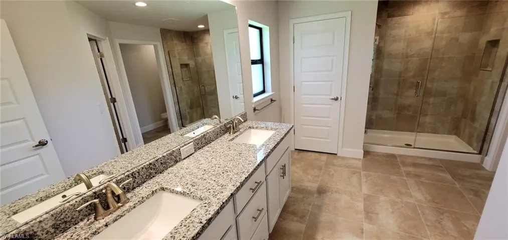 Primary Bathroom featuring tile patterned flooring, a shower with door, toilet, and dual bowl vanity