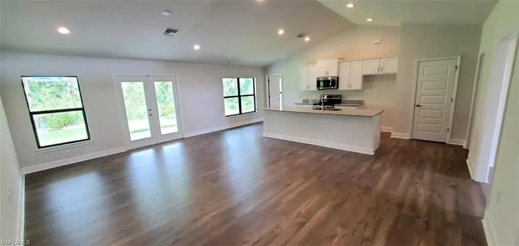Kitchen featuring white cabinetry, french doors, dark hardwood / wood-style floors, appliances with stainless steel finishes, and a center island with sink