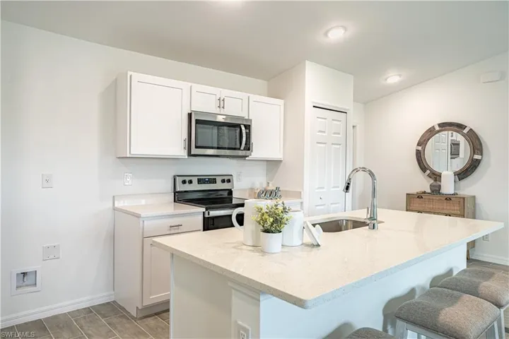 Kitchen featuring stainless steel appliances, white cabinetry, light stone countertops, a breakfast bar, and a center island with sink