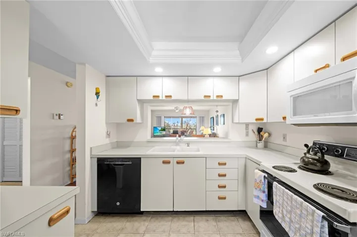 Kitchen with white appliances, light countertops, white cabinetry, a tray ceiling, and crown molding