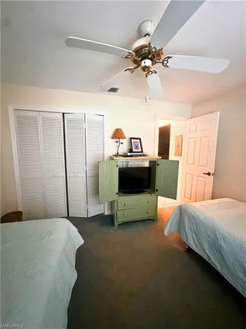 Carpeted bedroom featuring ceiling fan and a closet