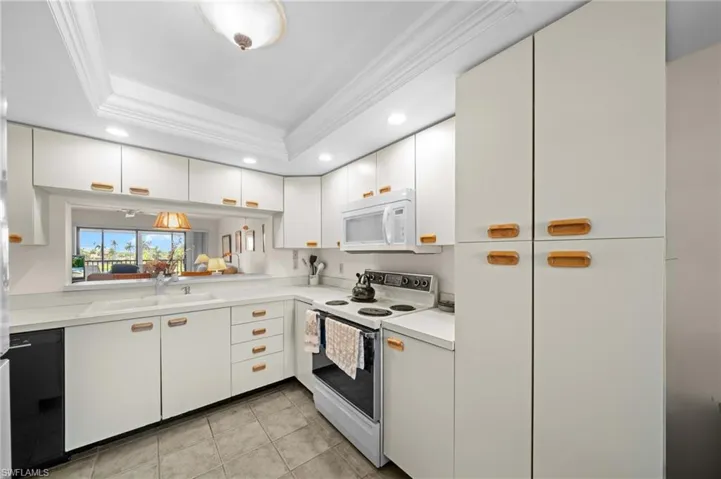 Kitchen with white appliances, light countertops, white cabinetry, a tray ceiling, and crown molding