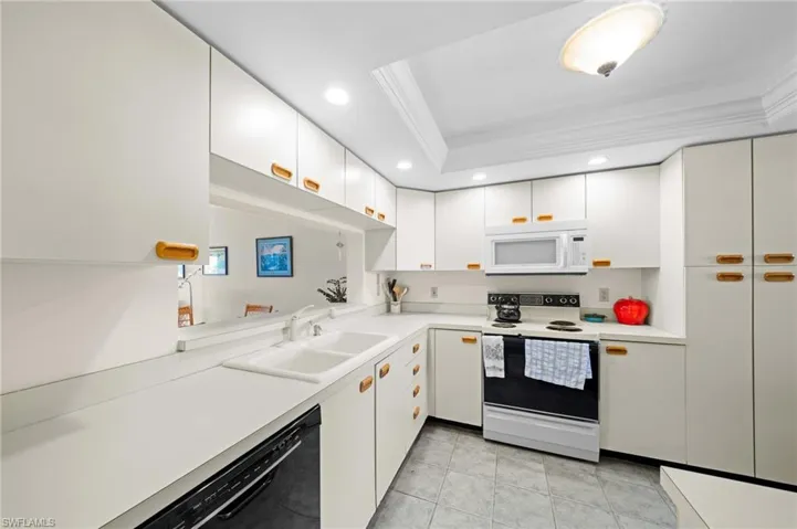 Kitchen featuring white appliances, light countertops, a raised ceiling, white cabinetry, and recessed lighting