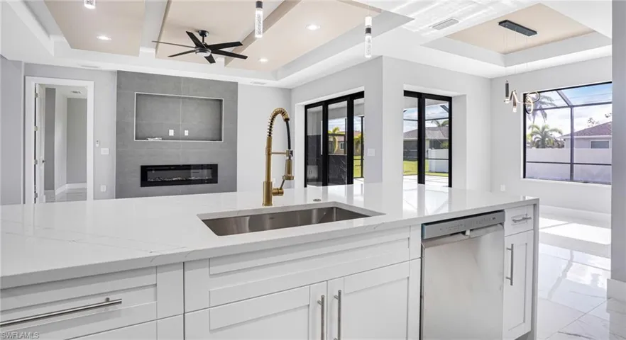 Kitchen featuring stainless steel dishwasher, white cabinetry, sink, and a tray ceiling
