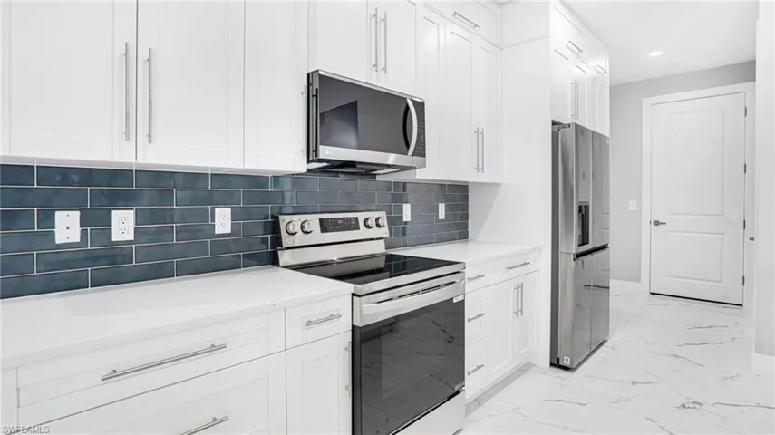 Kitchen with white cabinets, light stone countertops, backsplash, and appliances with stainless steel finishes