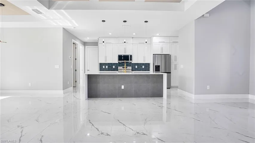 Kitchen featuring stainless steel appliances, a center island with sink, pendant lighting, backsplash, and white cabinetry