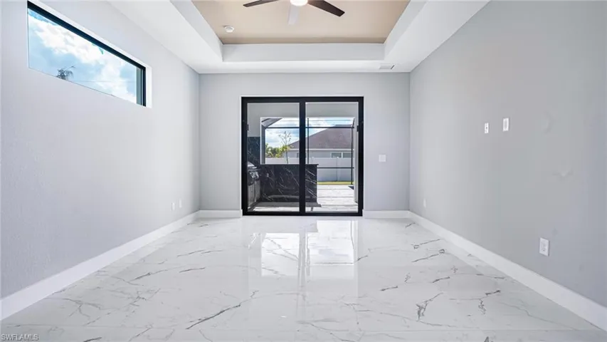 Unfurnished room featuring ceiling fan, plenty of natural light, and a tray ceiling