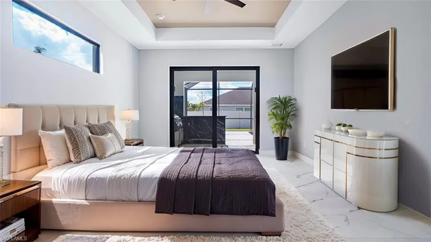 Bedroom featuring ceiling fan, access to exterior, multiple windows, and a tray ceiling