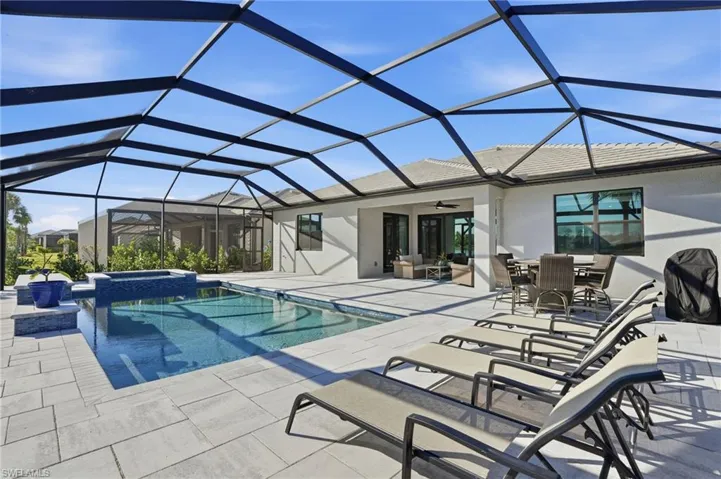 View of pool with glass enclosure, a sunroom, outdoor dining area, and a pool with connected hot tub