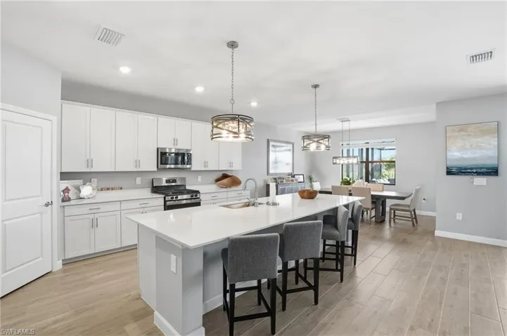 Kitchen featuring stainless steel appliances, pendant lighting, light wood-style floors, a kitchen island with sink, and recessed lighting