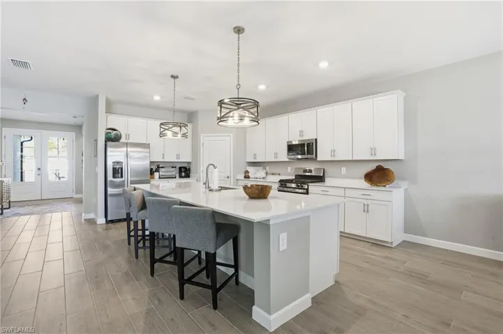Kitchen featuring a breakfast bar, appliances with stainless steel finishes, white cabinetry, an island with sink, and pendant lighting